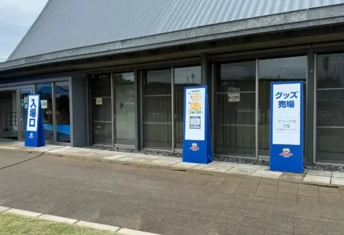 スポーツ会場の入口に設置されたプラダン看板。入場口やグッズ売場の案内サインとして活用されている屋外案内看板