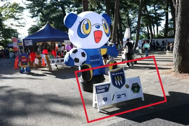 スタジアム入口に設置されたマッチデーパネル。試合日程・対戦カードを表示し、大型エアマスコットと組み合わせて来場者の案内や記念撮影スポットとして活用されている会場装飾。