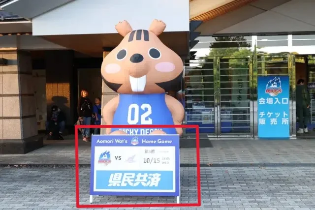 スタジアム入口に設置されたマッチデーパネル。試合日程・対戦カードを表示し、大型エアマスコットと組み合わせて来場者の案内やフォトスポットとして活用されるスポーツイベント装飾。