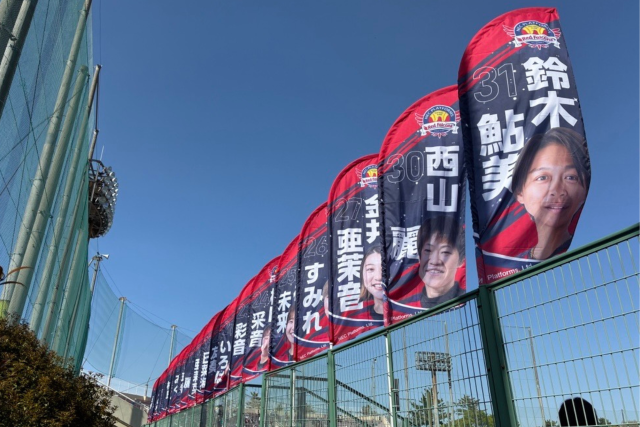 NECレッドファルコンズの選手写真と名前をデザインしたセイルバナーを、屋外フェンス沿いに連続設置した装飾事例。