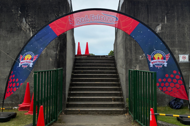 NECレッドファルコンズのロゴとチームカラーをデザインしたサークルゲートバナーを、会場入口の階段前に設置した装飾事例。